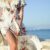 Fashion - woman walking on seaside while holding woven bag