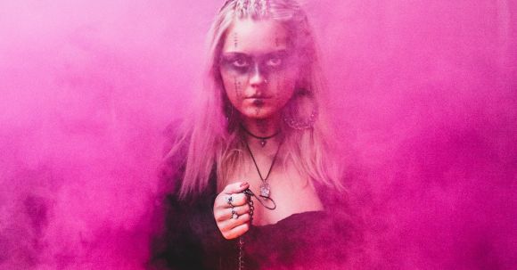 Power Dressing - Blond scary woman with makeup and in dress holding glowing lamp while standing in pink colored smoke looking at camera